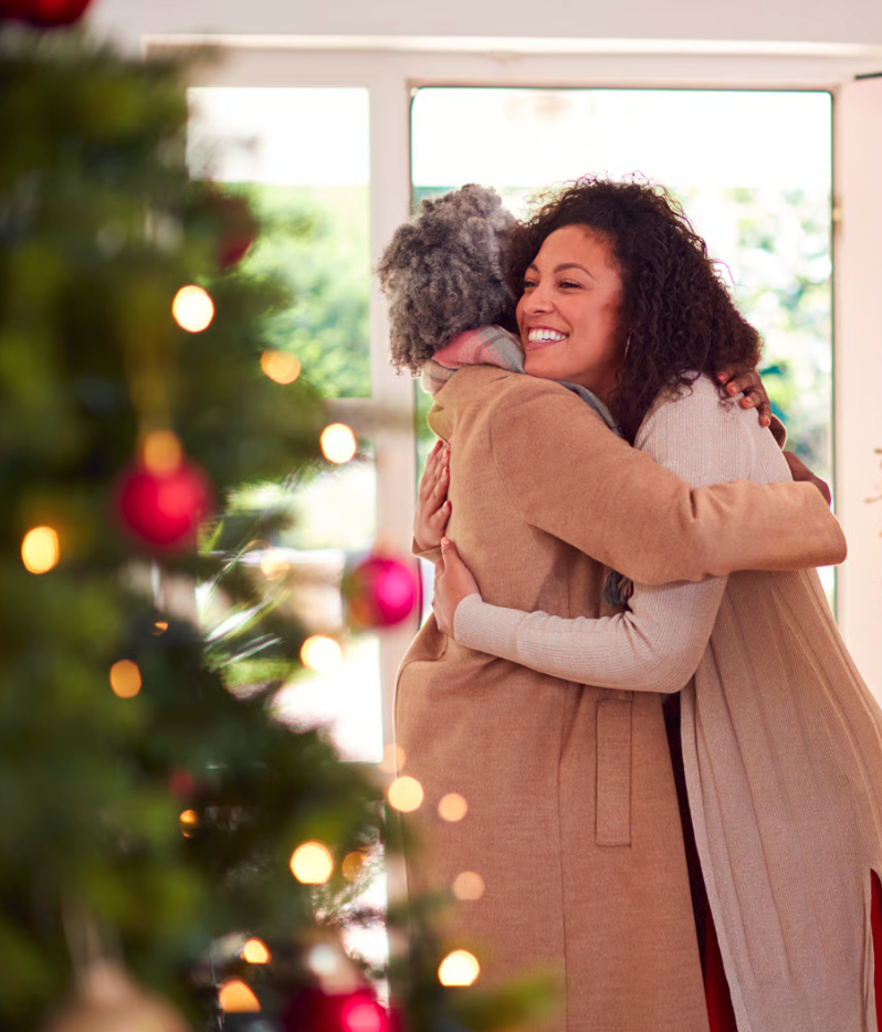 two women embracing in front of a christmas tree